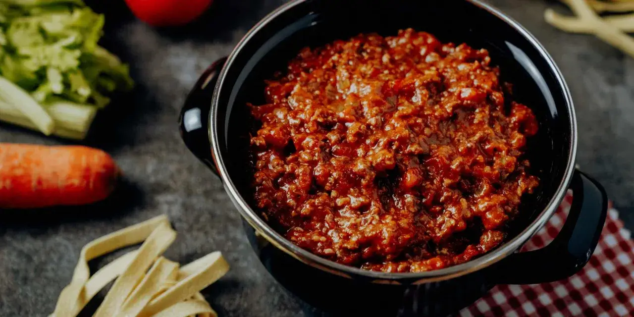 Herzhaftes Ragu in einem Topf, bereit für ein köstliches Ragu Rezept. Daneben liegen frische Zutaten wie Karotten und Sellerie.