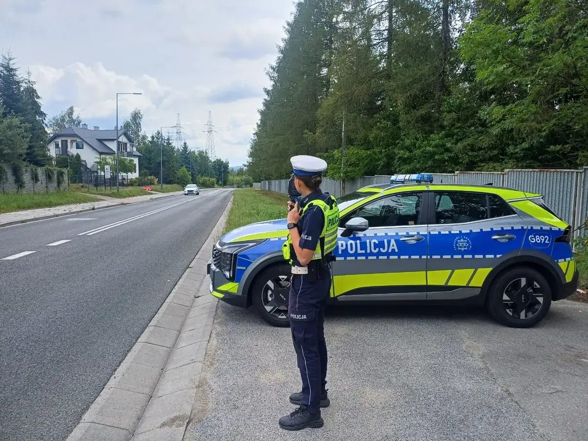 Policjantka kontroluje ruch drogowy obok radiowozu. Działania mają na celu zapobieganie **jeździe pod wpływem** alkoholu lub innych substancji.