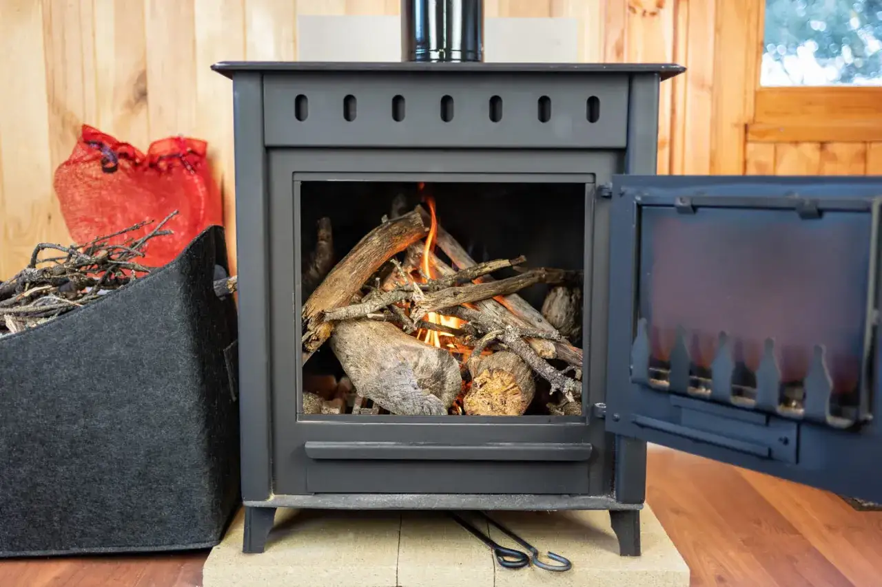 Poêle à bois crépitant, la chaleur du feu de bois réchauffe la pièce. Des bûches et brindilles sont prêtes à être ajoutées.