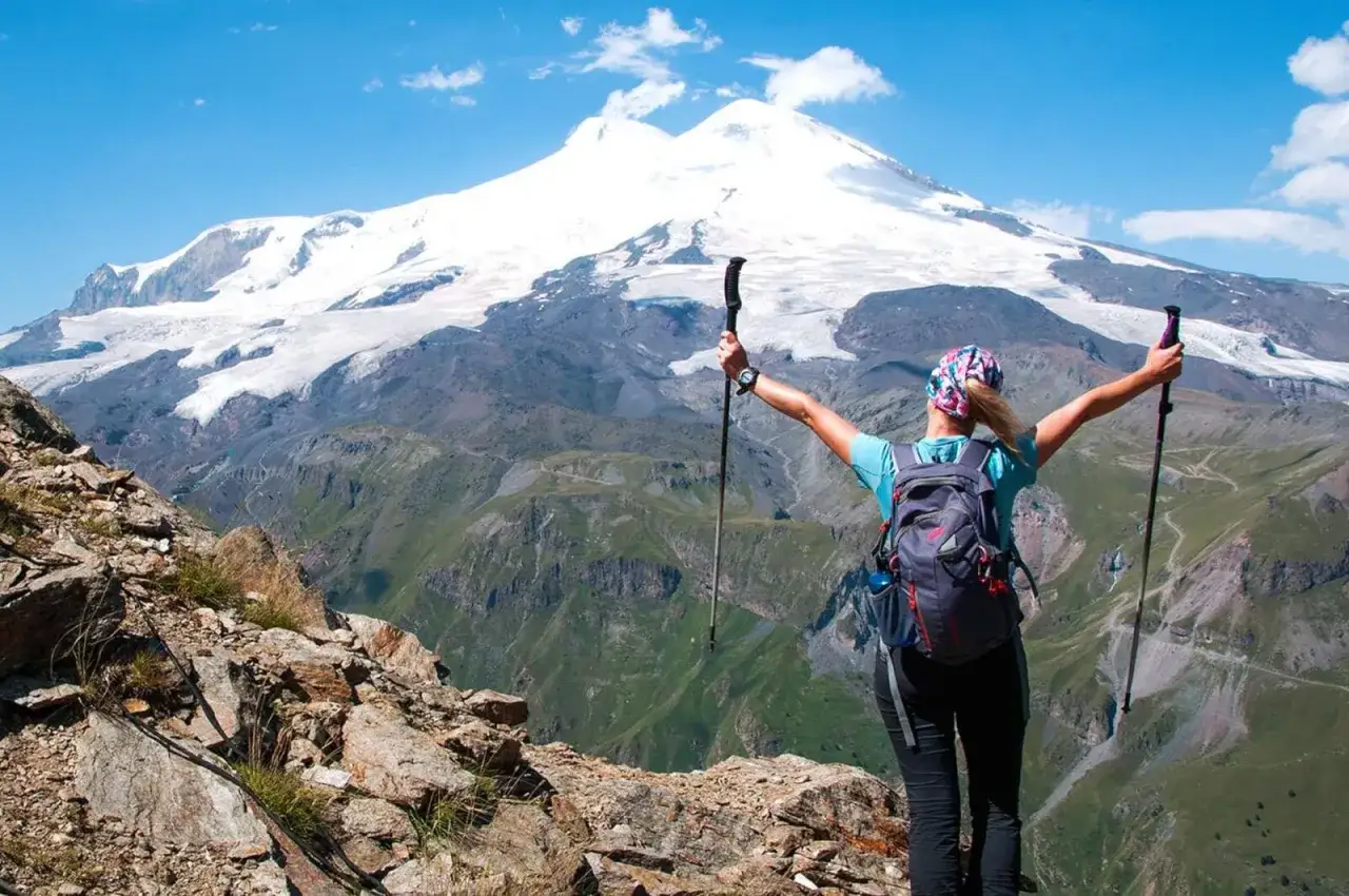 Turystka z plecakiem i kijkami wspina się na Elbrus szczyt, podziwiając majestatyczny widok.