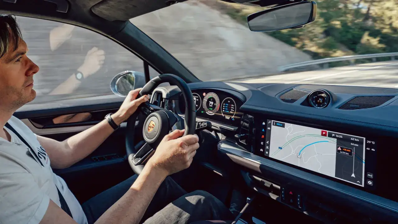 Mężczyzna prowadzi Porsche Cayenne Turbo, trzymając kierownicę. Na ekranie nawigacji widoczna jest trasa.