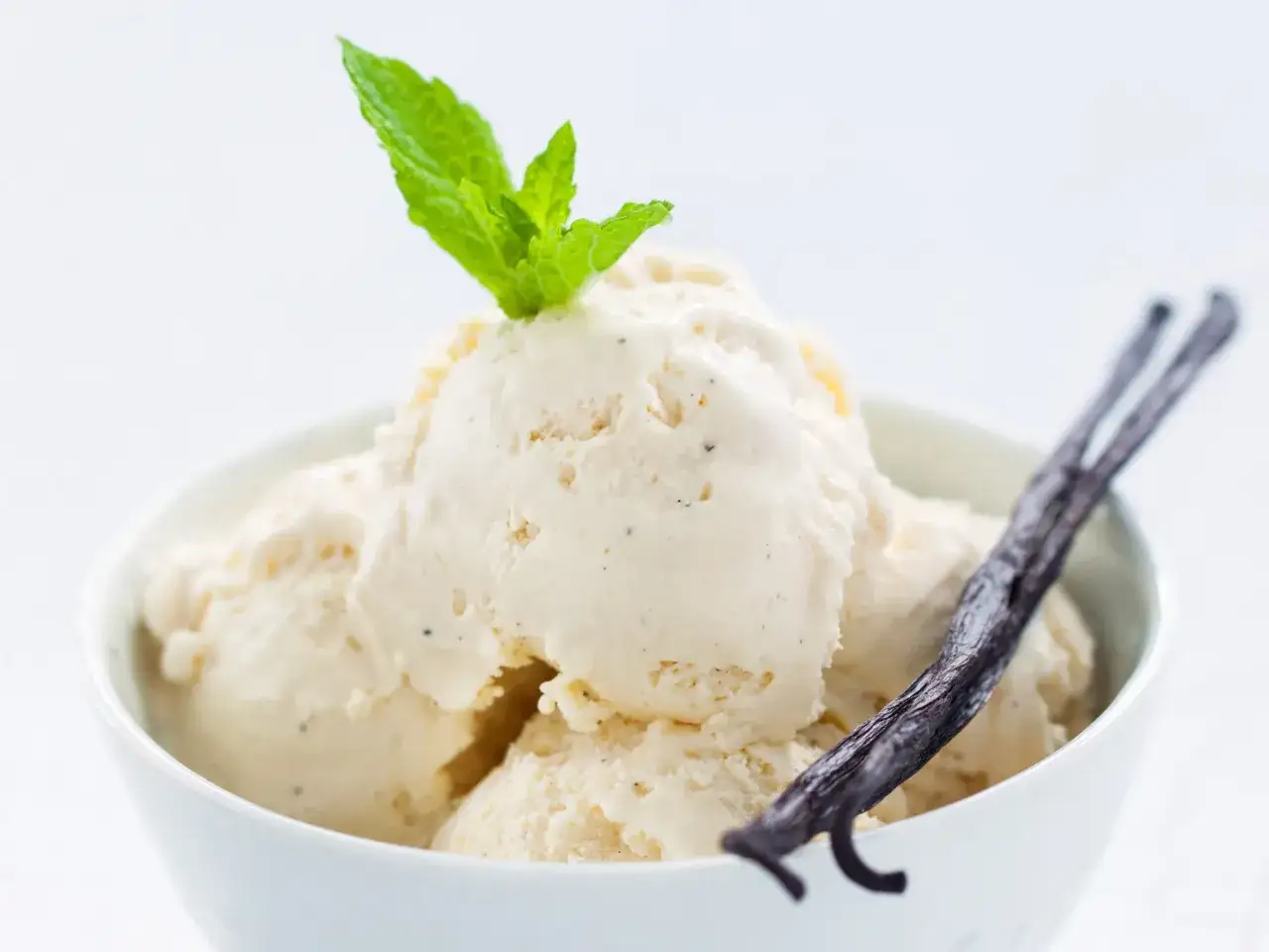 Kremowe lody domowe z wanilią i miętą, ozdobione laską wanilii.