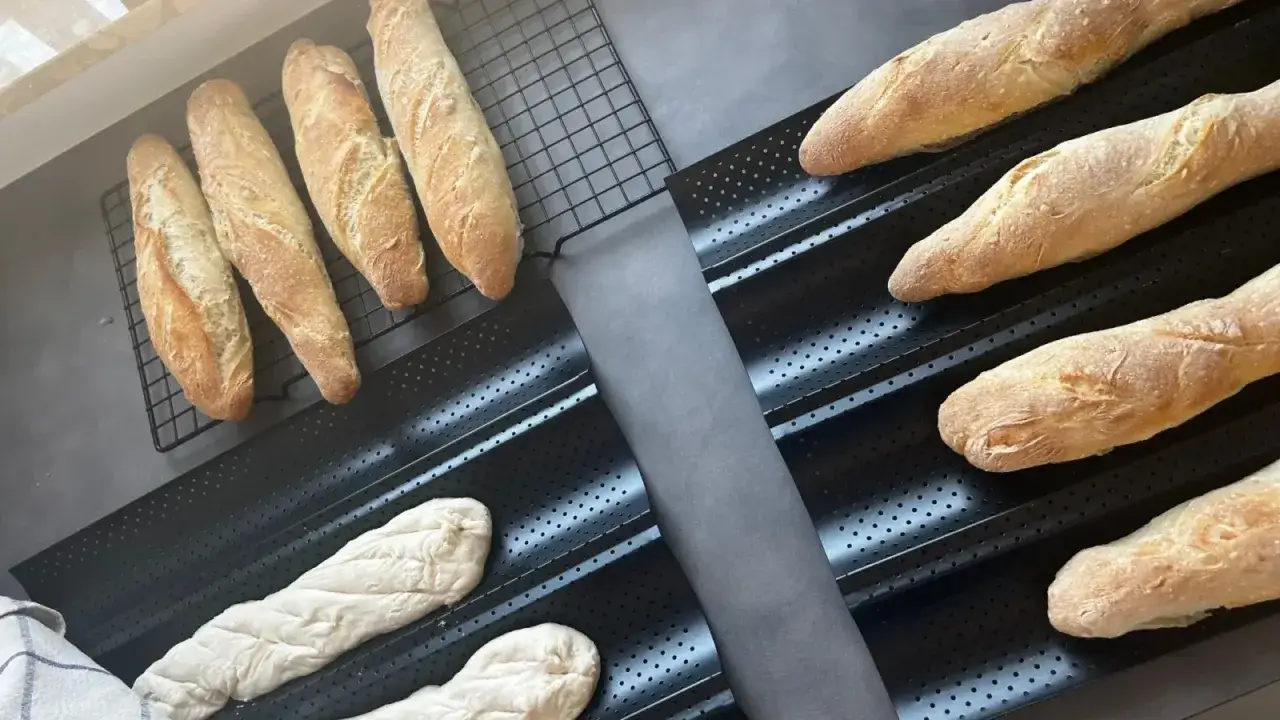 Gotowe do pieczenia bagietki po francusku, niektóre już upieczone na kratce, inne czekają w formie.