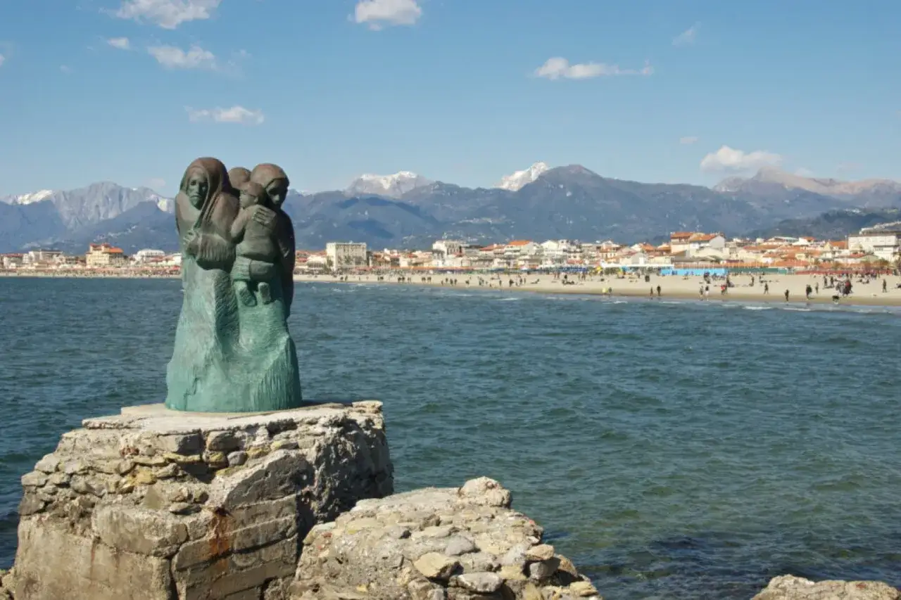 Sculpture de famille sur un rocher, face &agrave; la plage anim&eacute;e de via Reggio. Montagnes enneig&eacute;es en arri&egrave;re-plan.