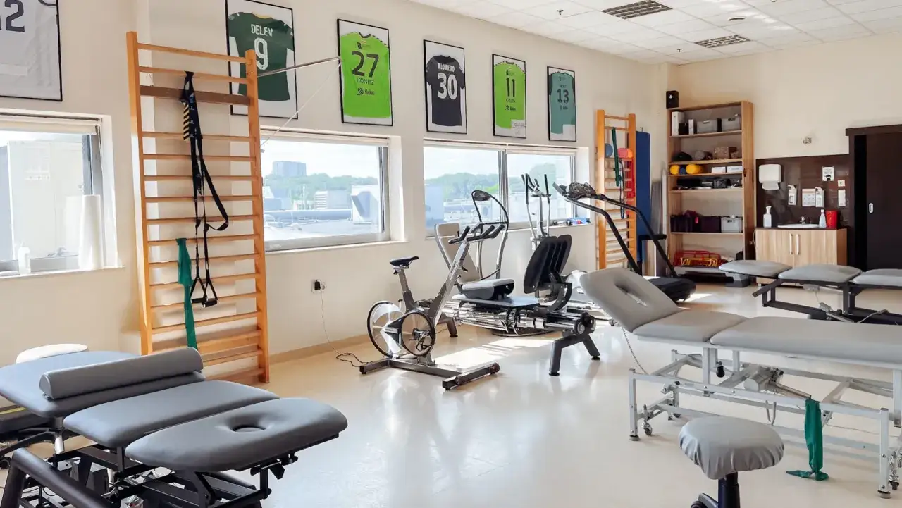 Sala rehabilitacyjna z ławkami, rowerami stacjonarnymi i drabinką gimnastyczną.