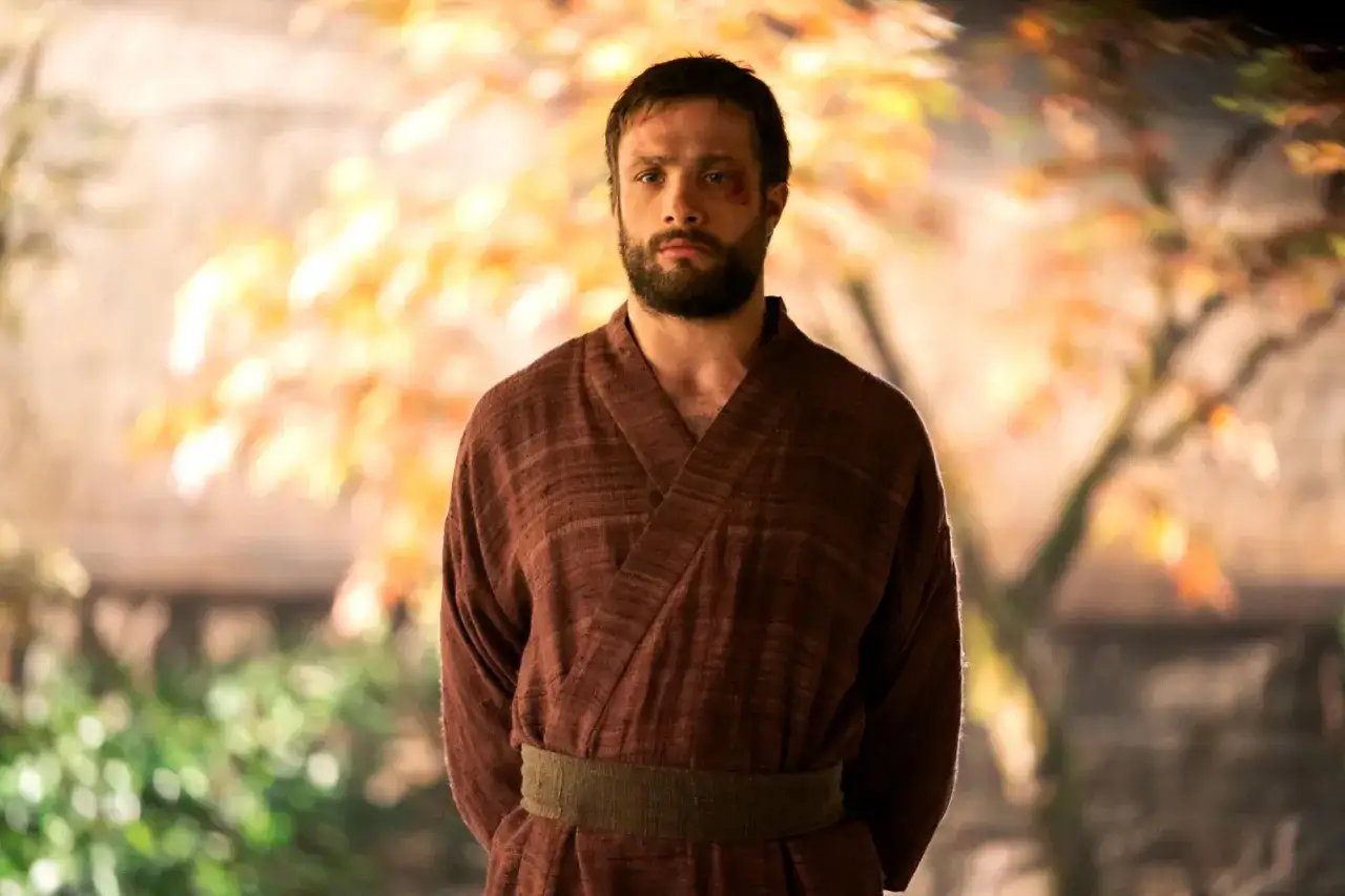 Cosmo Jarvis står i en brun kimono med ett grönt bälte. Bakgrunden är suddig med höstfärger.