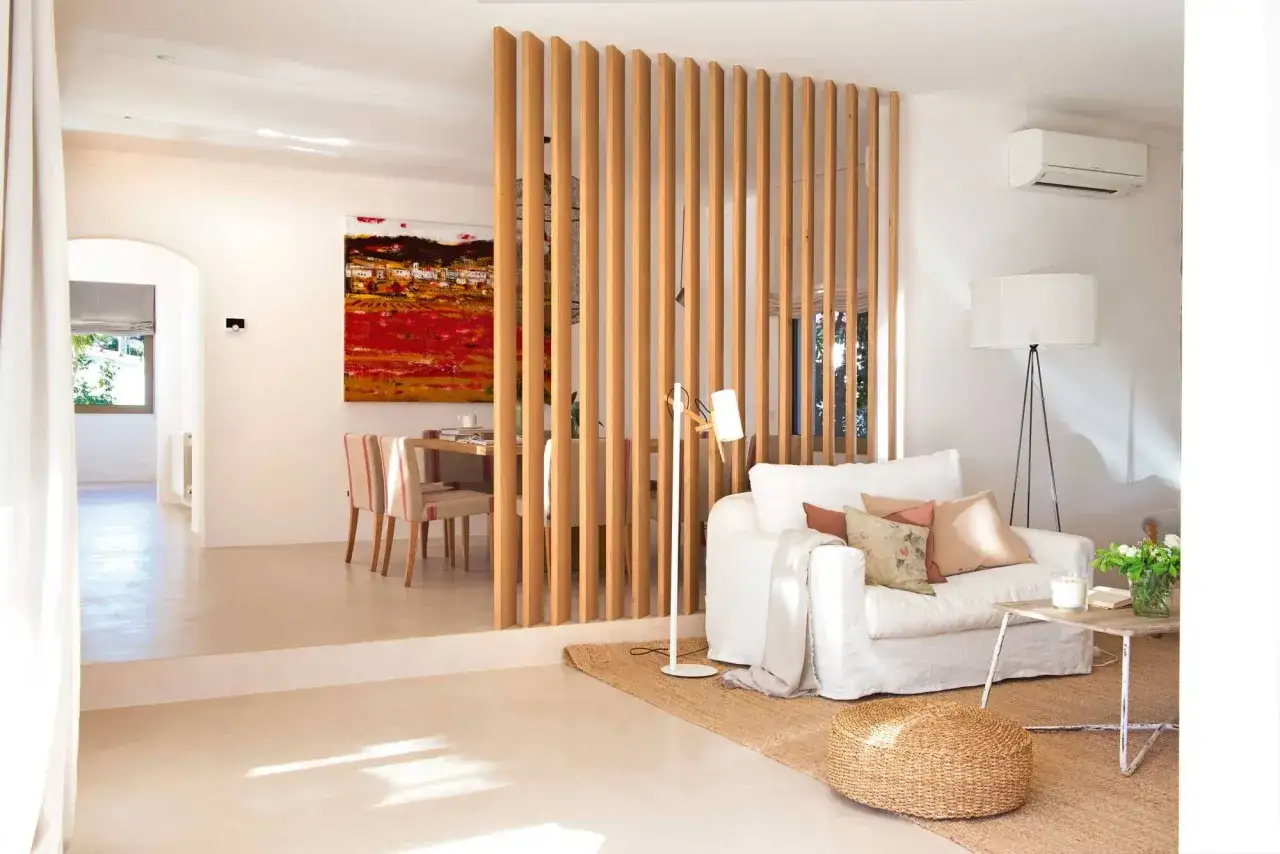 Un elegante salón comedor dos ambientes, separado por una celosía de madera. Sofá blanco, mesa de centro rústica y cuadro vibrante.