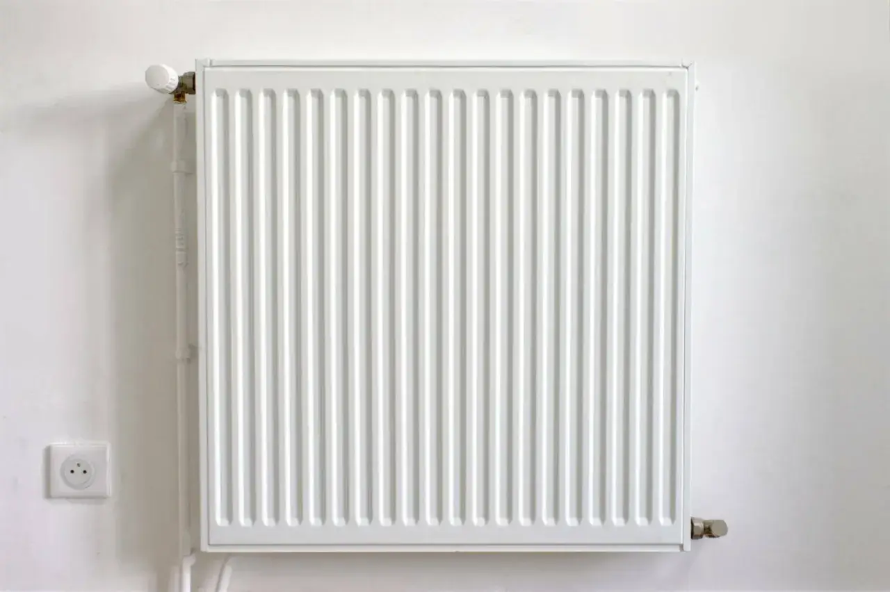 Radiateur blanc moderne sur mur blanc, prêt à offrir le meilleur chauffage. Une prise électrique est visible à gauche.