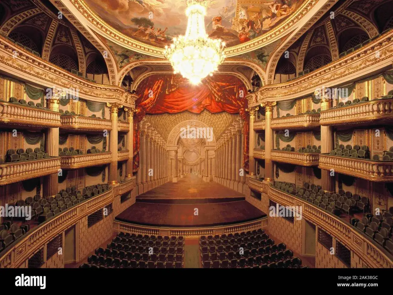 Wnętrze teatru z wieloma balkonami i rzędami siedzeń, ozdobione złotem i freskami na suficie. To największy teatr na świecie, gotowy na spektakl.