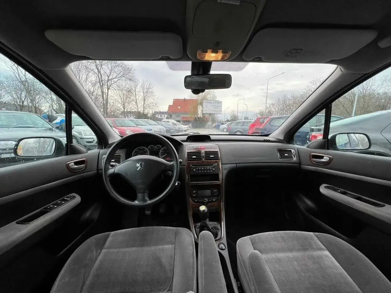 Wnętrze Peugeot 307 1.6 HDI. Widok na deskę rozdzielczą, kierownicę z logo lwa, dźwignię zmiany biegów i fotele.
