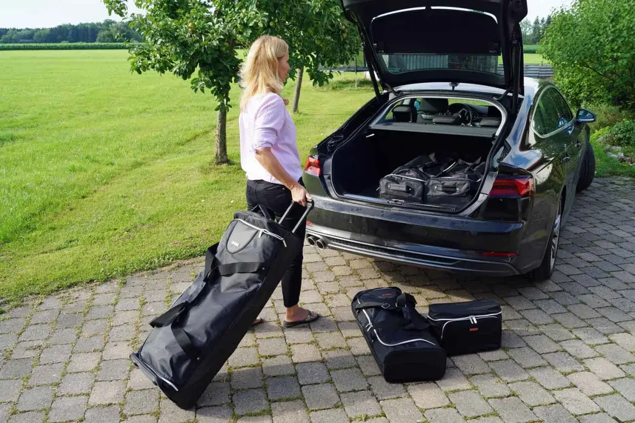 Frau packt Koffer für den Roadtrip. Gepäckstücke liegen bereit, um im Kofferraum verstaut zu werden.
