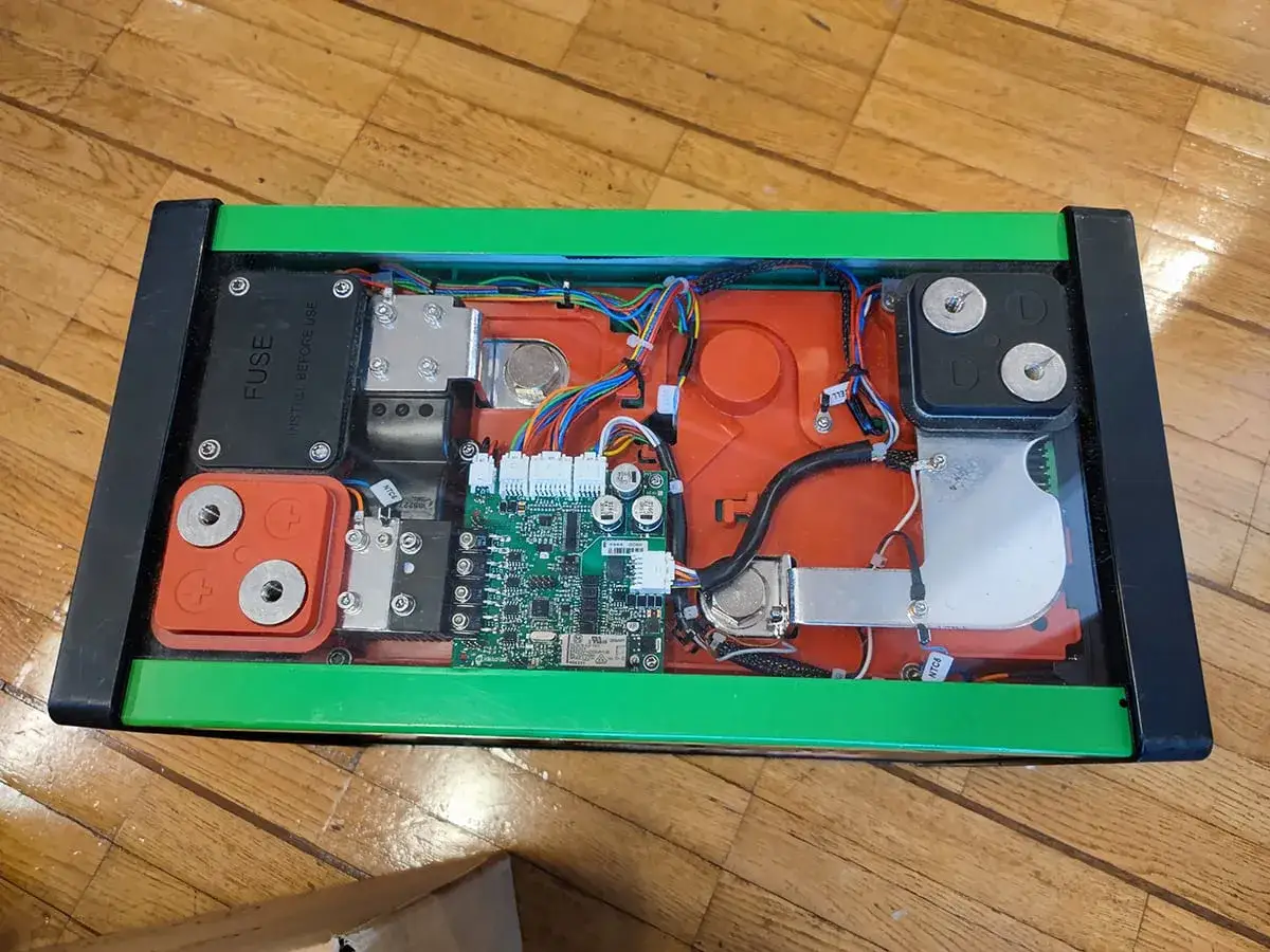 Öppen låda med grönt chassi visar ett komplext bms batteri med kretskort, kablar och anslutningar.