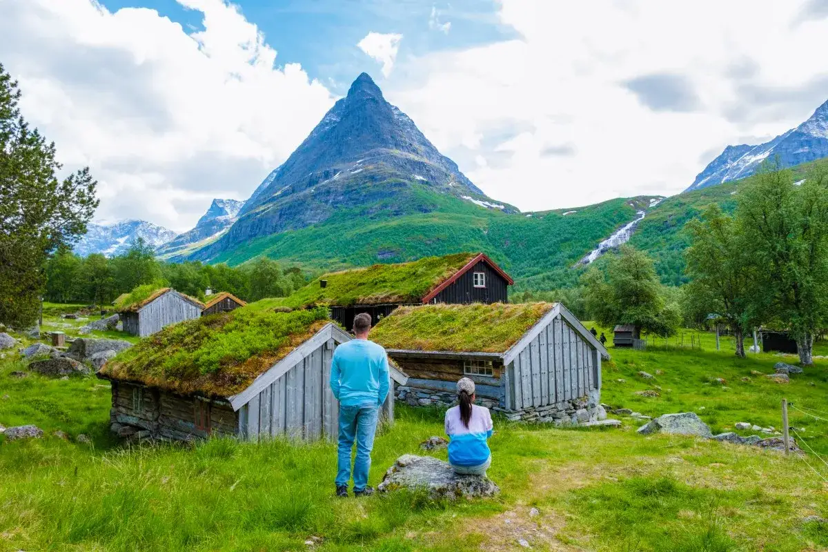Para zwiedzająca tradycyjne chaty z zielonymi dachami w Norwegii. Planujesz podróż? Sprawdź norwegia zasady wjazdu.