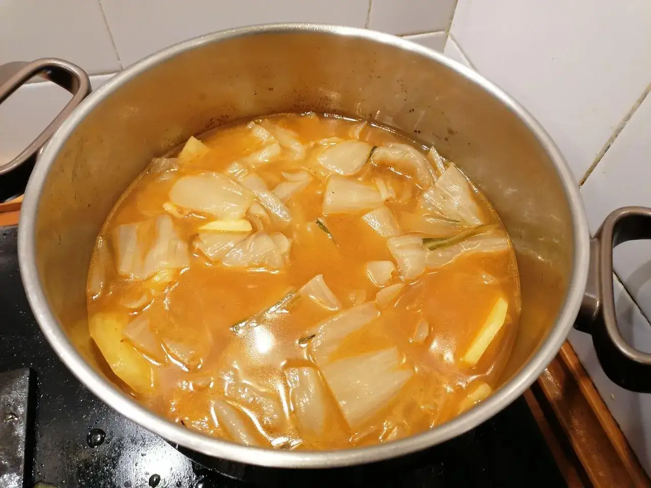 Olla con guiso de pencas de acelgas y patatas, con un caldo anaranjado y trozos de verdura tierna.