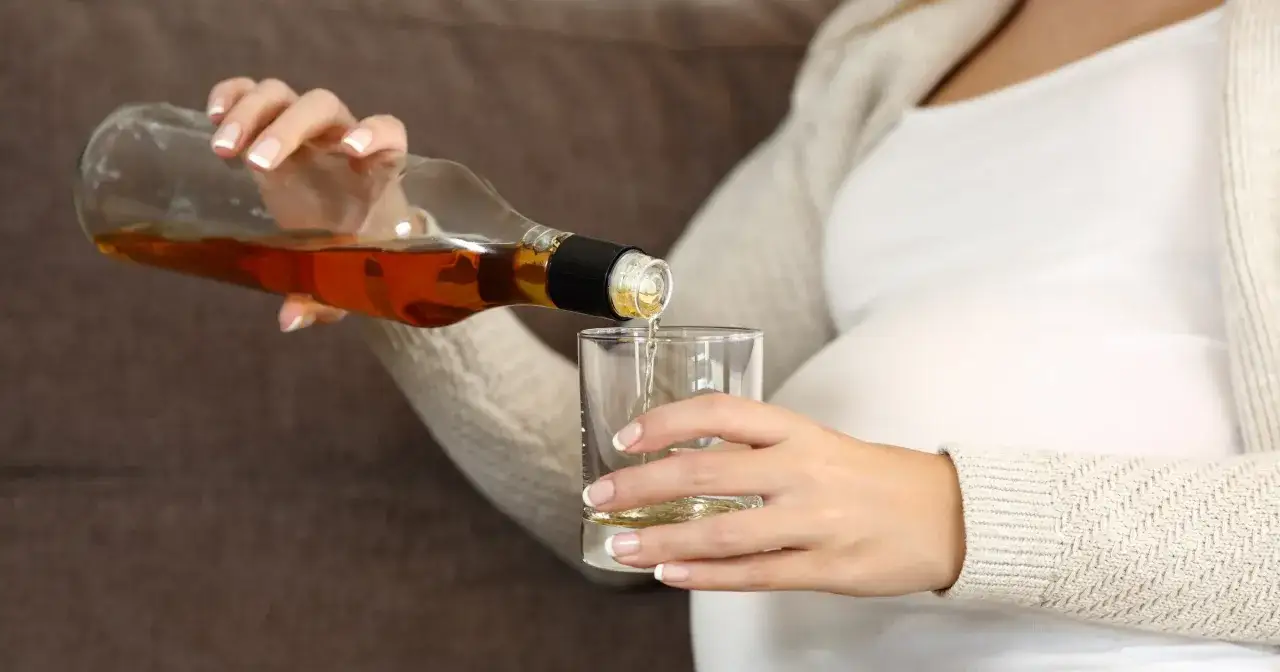 Kobieta w ciąży nalewa alkohol do szklanki. To może prowadzić do zespołu FAS.
