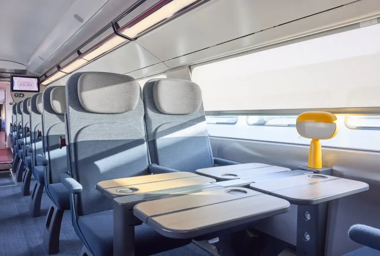 Wygodne siedzenia w wagonie TGV z rozkładanymi stolikami i lampką.