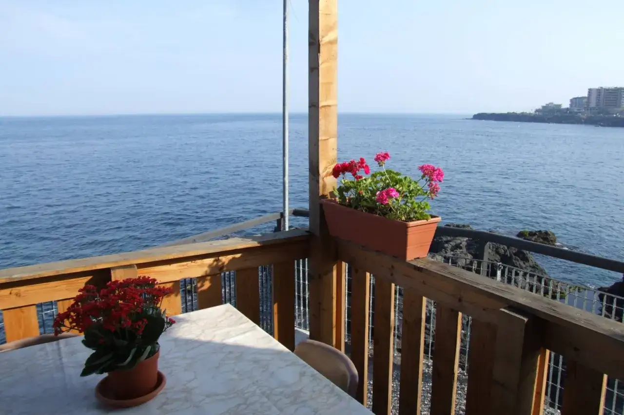 Balc&oacute;n con flores y vista al mar, ideal para visitar Sicilia.