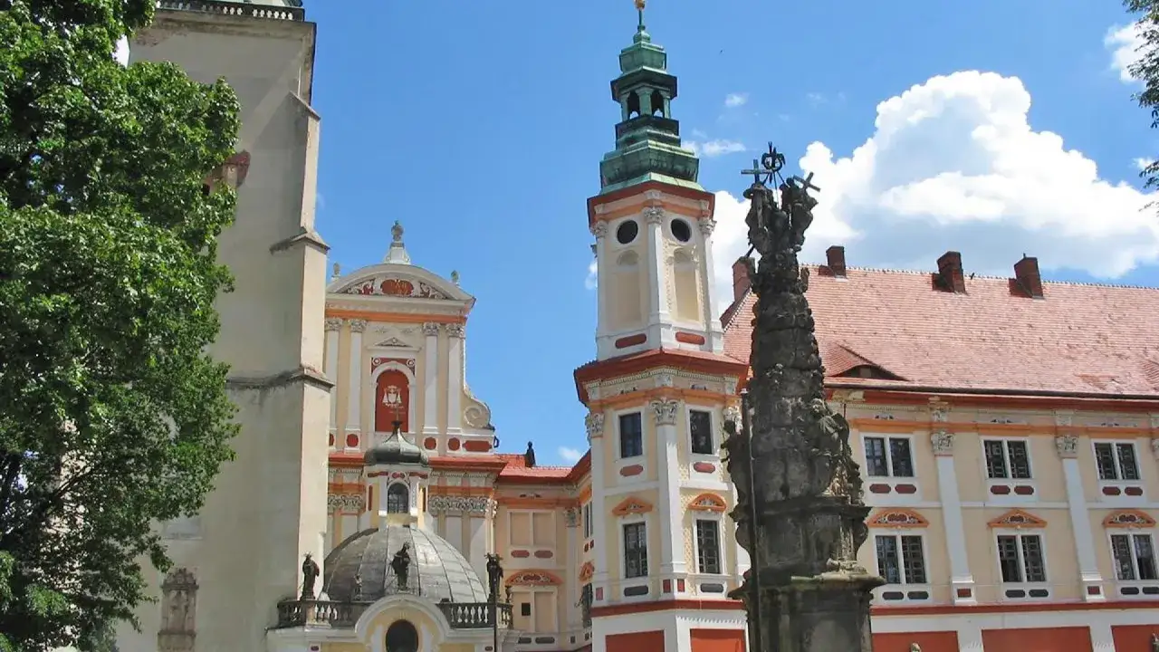 Zwiedzanie Henryków opactwo: barokowa architektura, wieża z zielonym hełmem, rzeźba na pierwszym planie i błękitne niebo.