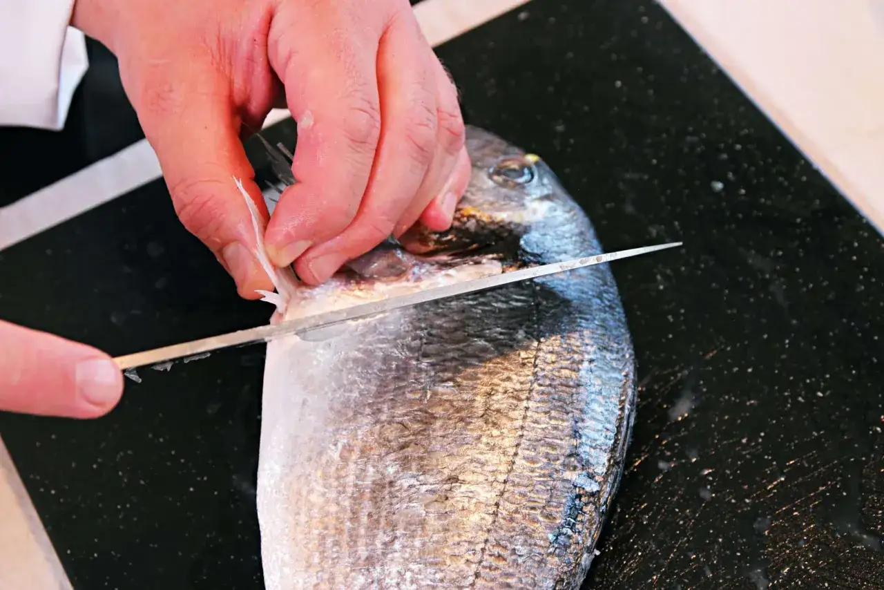 H&auml;nde filetieren einen frischen Fisch am Tisch mit einem scharfen Messer.