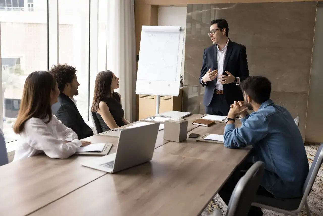A team meeting focused on ethical leadership, with a presenter discussing sales strategies on a whiteboard to attentive colleagues in a modern office.