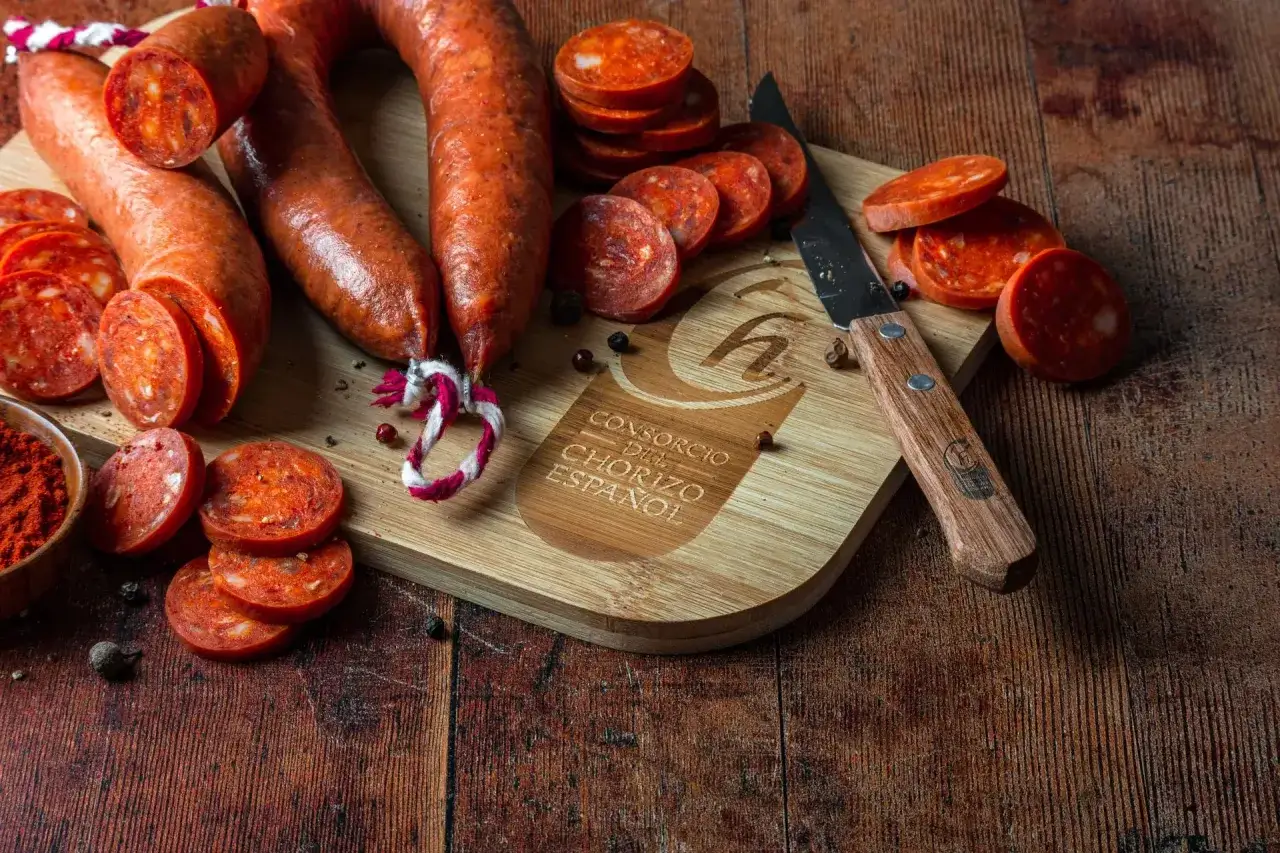 Kawałki chorizo na desce, obok nóż i miseczka z papryką. To jest właśnie chorizo, co to za przysmak!