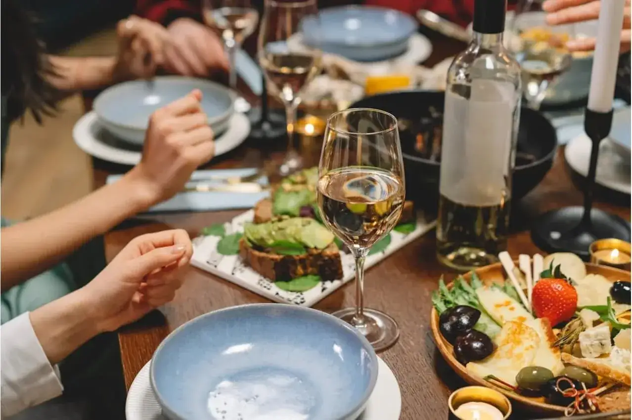 Un verre de vin blanc mi sec mi moelleux, une bouteille, des toasts à l'avocat et un plateau de fromages et fruits sur une table dressée pour un repas convivial.