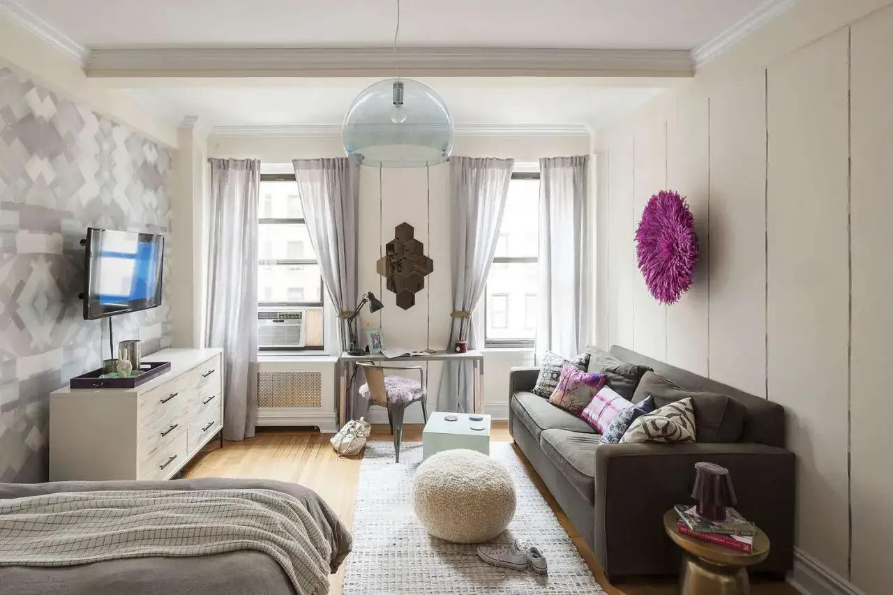 Am&eacute;nagement studio fonctionnel avec lit, canap&eacute;, bureau et rangements. D&eacute;coration murale g&eacute;om&eacute;trique et coussins color&eacute;s.
