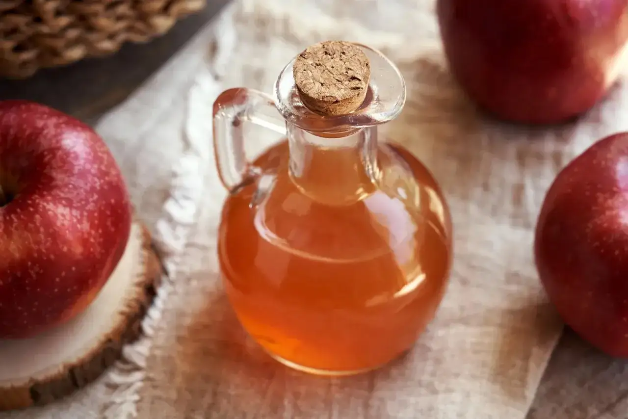 Bouteille de vinaigre de cidre, entourée de pommes rouges. Un remède naturel pour la prostate ?