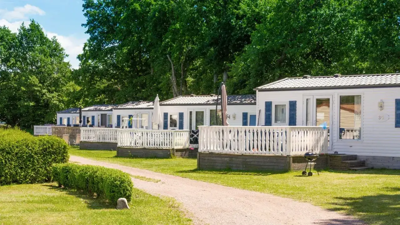 Rad av vita stugor med altaner och grill vid Ekerums Resort. Grönskande träd och buskar.