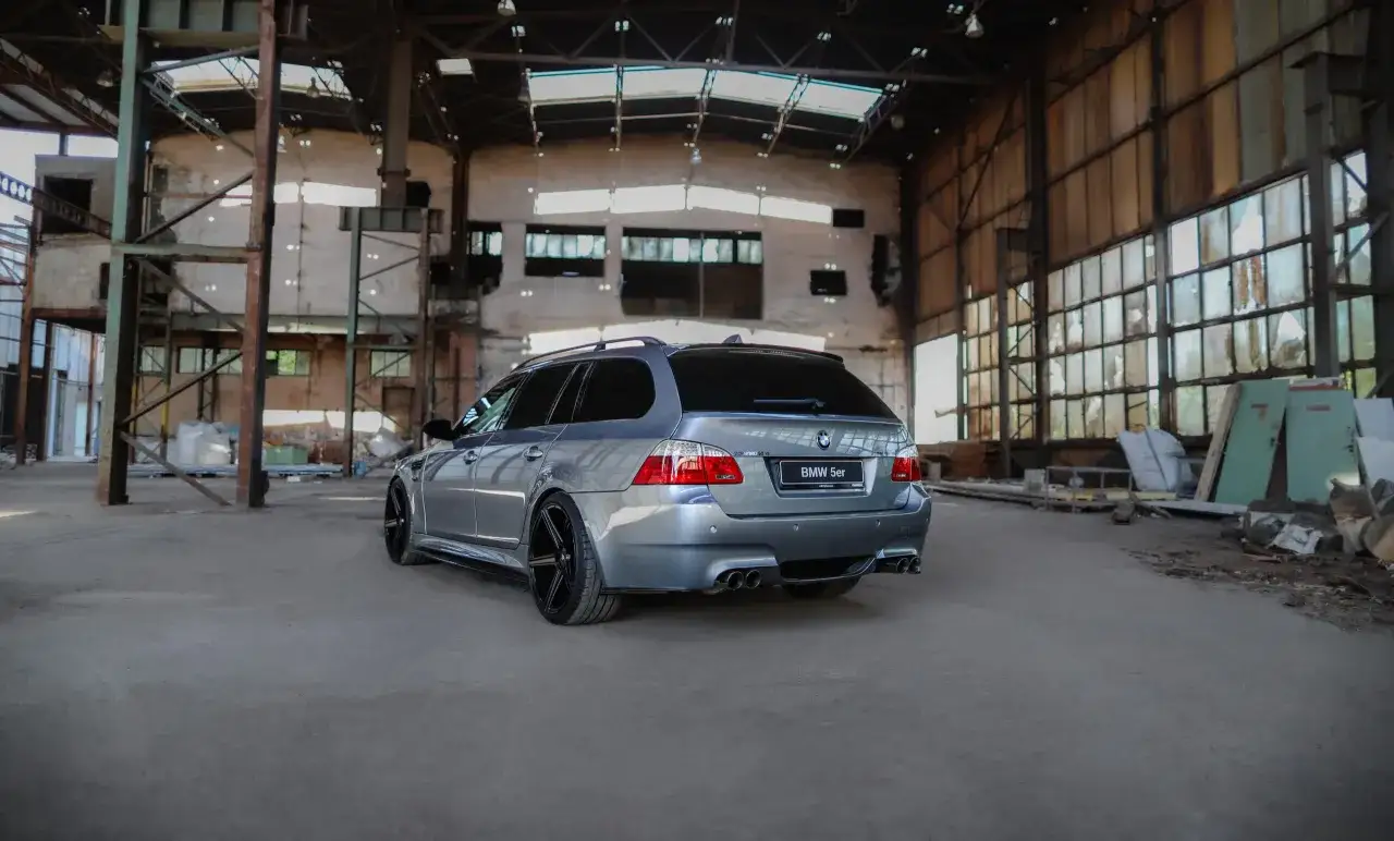 Szare BMW E61 z czarnymi felgami stoi w opuszczonej hali fabrycznej.