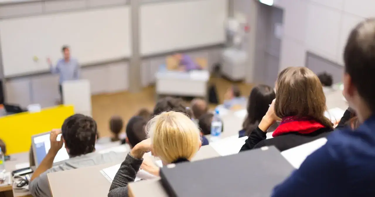 Wykład na studiach dla dorosłych. Słuchacze siedzą w auli, jeden z nich korzysta z laptopa.