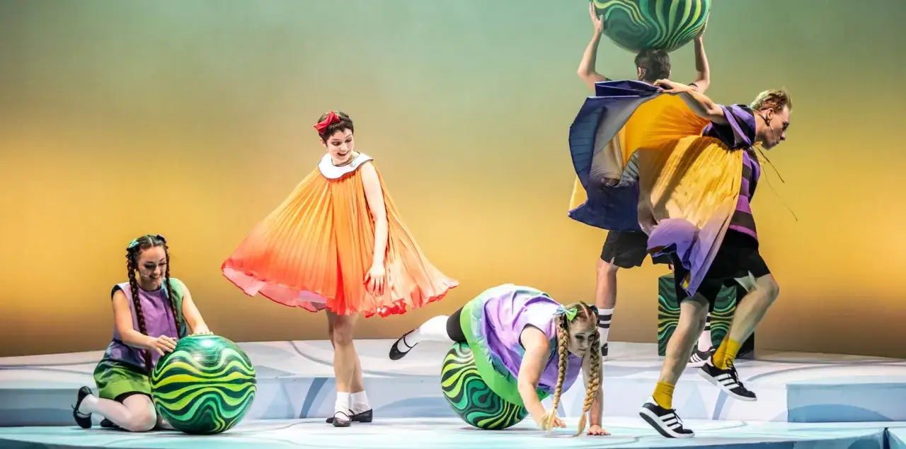 Dzieci na scenie bawią się wielkimi piłkami. To właśnie jest teatr – miejsce, gdzie dzieją się niezwykłe rzeczy!