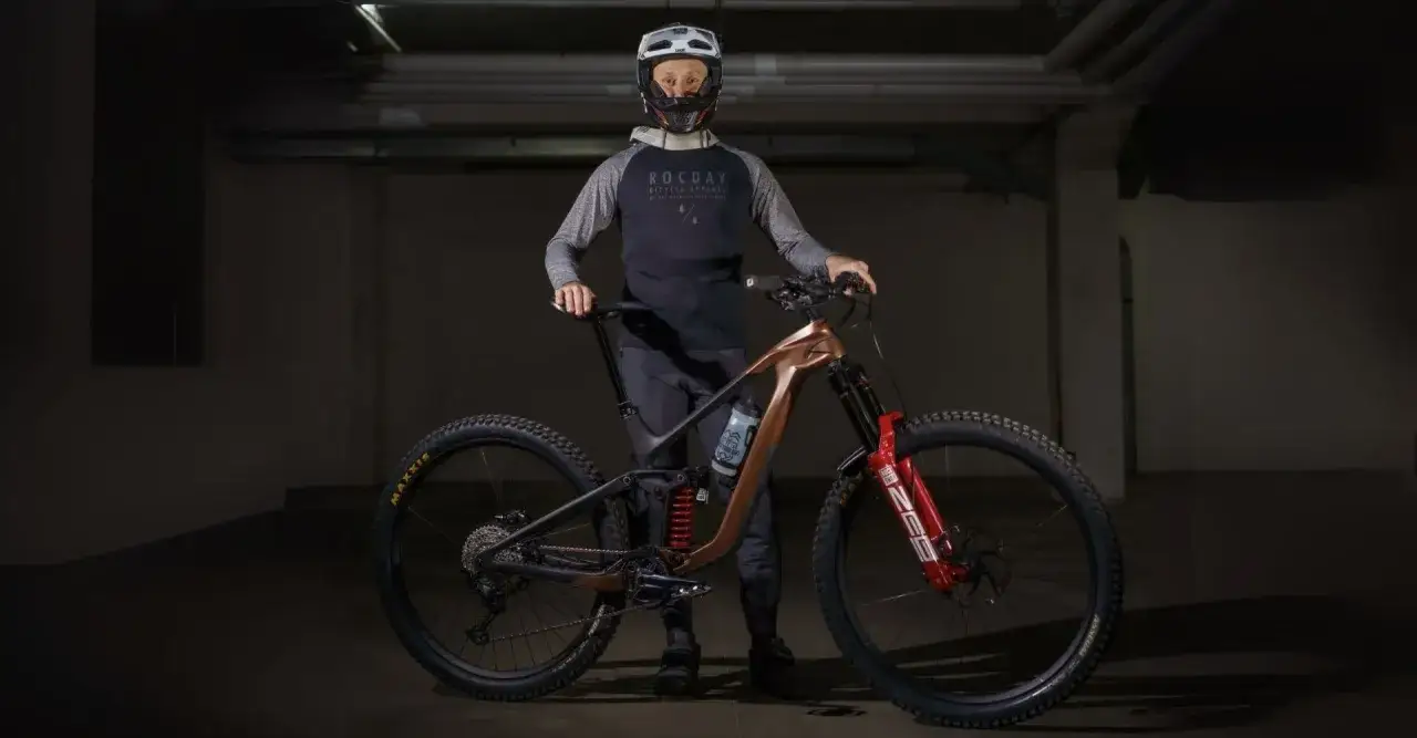 Kolarz w kasku i odzieży rowerowej prezentuje nowoczesny rower mtb. To sprzęt do ekstremalnej jazdy, co to znaczy, że jest gotowy na każde wyzwanie.