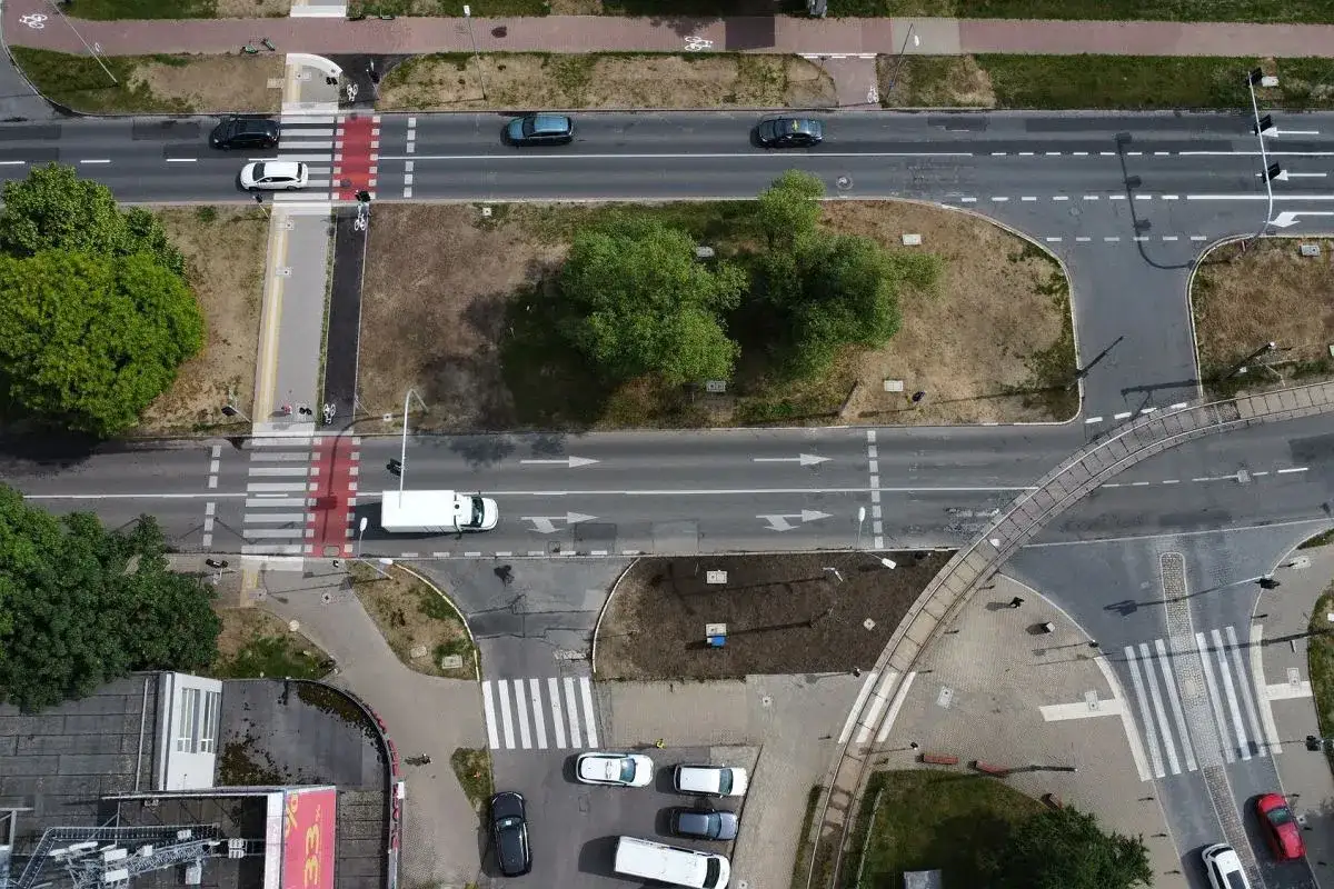 Skrzyżowanie z pasami dla pieszych i rowerzystów. Widać samochody i białą furgonetkę, a także sygnalizację świetlną.