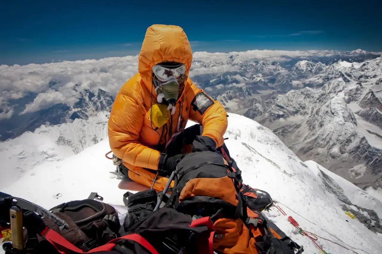 Alpinista w pomarańczowym kombinezonie z maską tlenową na szczycie Mount Everest, gdzie wysokość sięga 8848 m. Niesamowity widok na góry.
