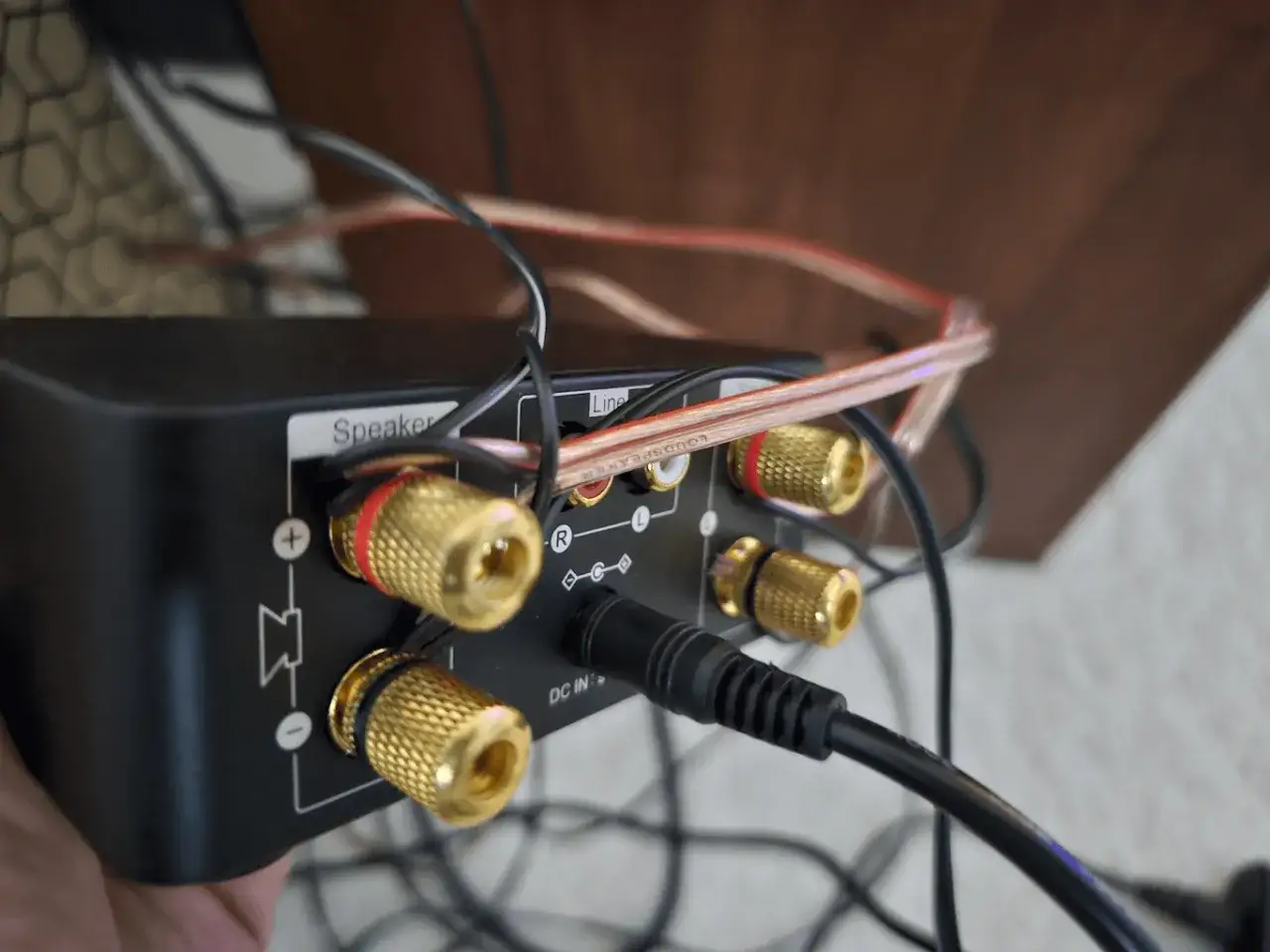 Złącza głośnikowe i wejście zasilania DC w czarnym wzmacniaczu. Widoczne są r&oacute;wnież kable audio, w tym wyjście liniowe audio.