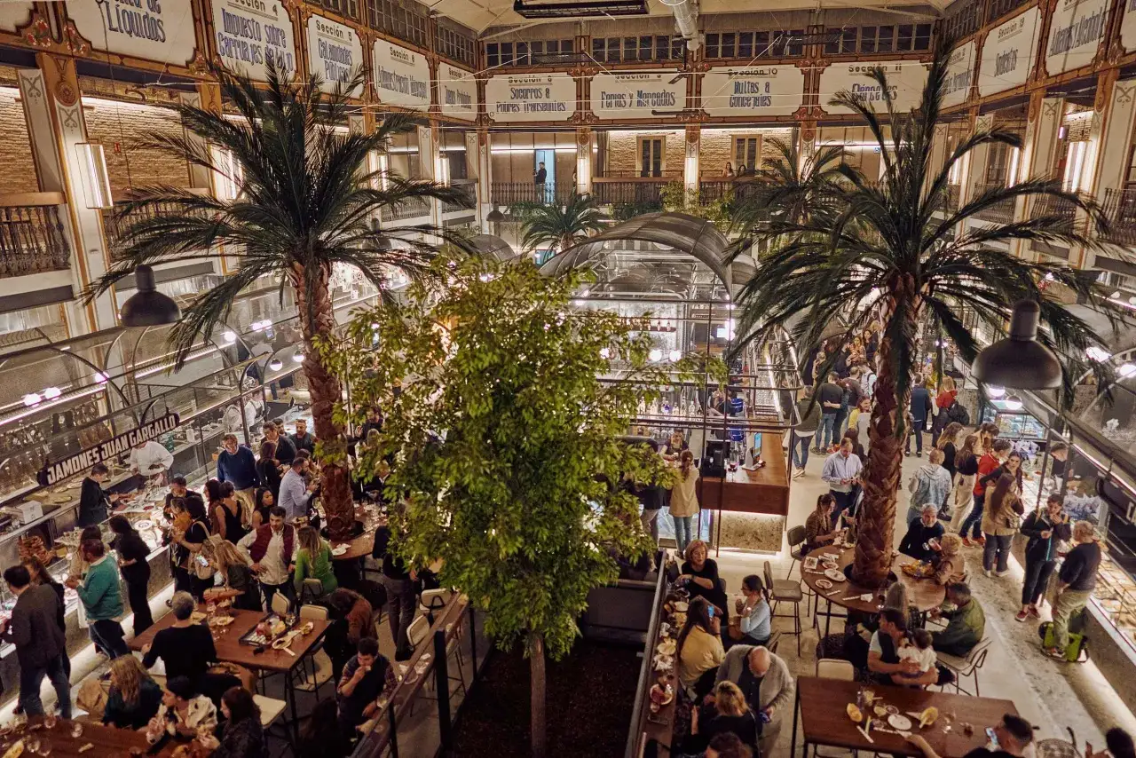 Gente disfrutando en un animado mercado de la imprenta, con palmeras y puestos de comida.