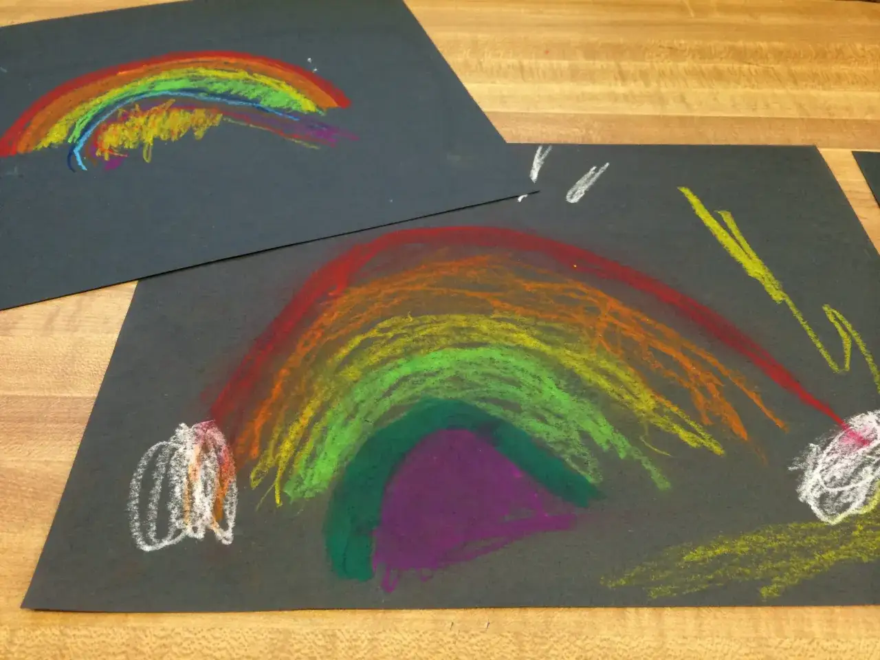Kinder malen auf schwarzem Papier bunte Regenb&ouml;gen mit Kreide.