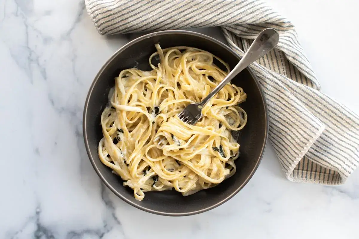 Un plat de pâtes fettuccine crémeuses, nappées d'une sauce mascarpone onctueuse, avec une touche de verdure. Un délice pour les amateurs de pâtes.