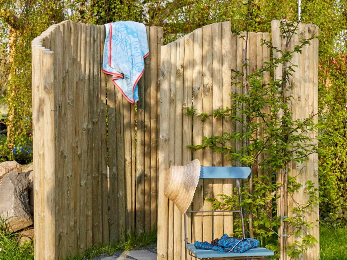 Holz-Sichtschutzwand mit Handtuch und Strohhut – tolle gartendusche ideen für entspannte Sommertage im Grünen.