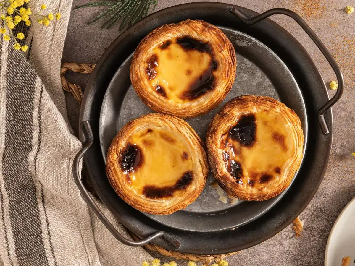 Tres deliciosos pasteles de Belém, con su crujiente hojaldre y crema dorada, listos para ser disfrutados.