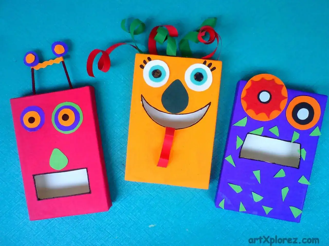 Creaturas divertidas hechas con manualidades con material reciclado: un robot rosa, un monstruo naranja sonriente y un alien morado.
