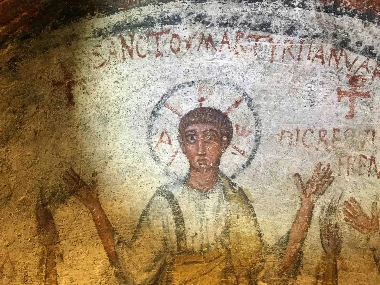 Affresco antico nella tomba di San Gennaro, raffigurante un martire con aureola e iscrizioni latine.