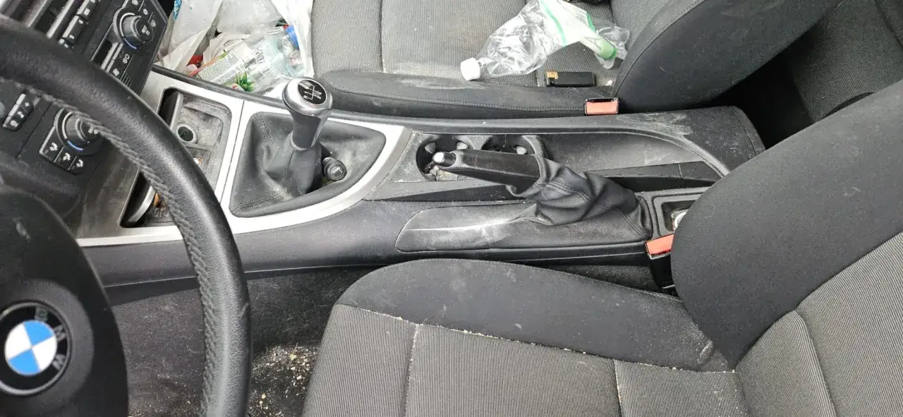 Wnętrze BMW 118d, widok na kierownicę, dźwignię zmiany biegów i hamulec ręczny. Widać ślady kurzu i bałaganu.