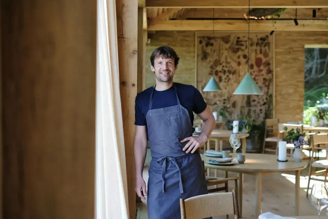 Uśmiechnięty kucharz w fartuchu, stojący w eleganckiej restauracji. Czy to on wie, dlaczego znany kucharz zamknął wszystkie swoje restauracje z dnia na dzień?