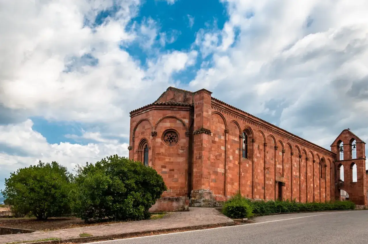 Antica chiesa in pietra rossa, con campanile e cielo nuvoloso. Il suo fascino evoca il nuoro significato di storia e spiritualità.