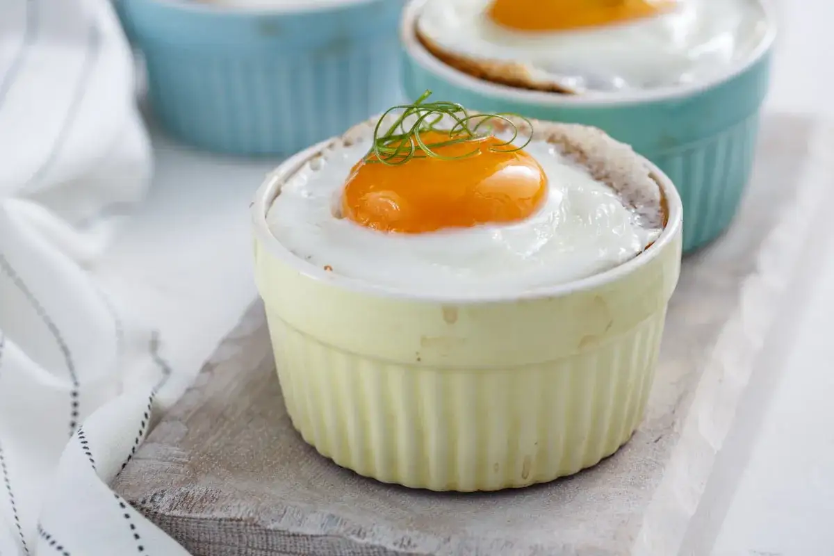 Un &oelig;uf cocotte bain-marie, un jaune d'&oelig;uf parfait sur un lit de blanc, garni d'une touche de verdure.