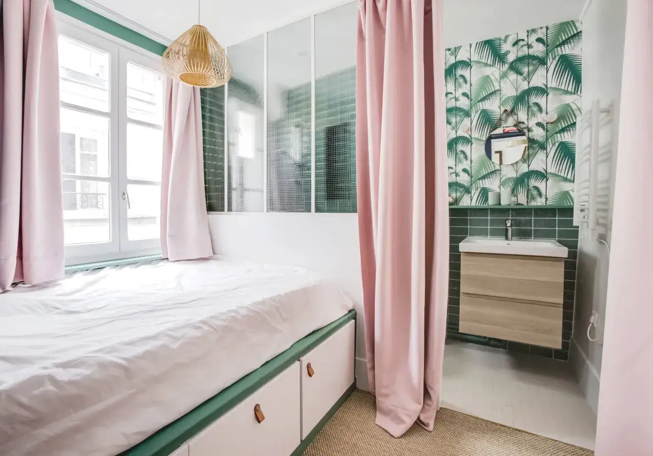 Une ado s&eacute;parer une petite chambre en deux avec des rideaux roses. Un coin lit et un coin salle de bain avec papier peint tropical.