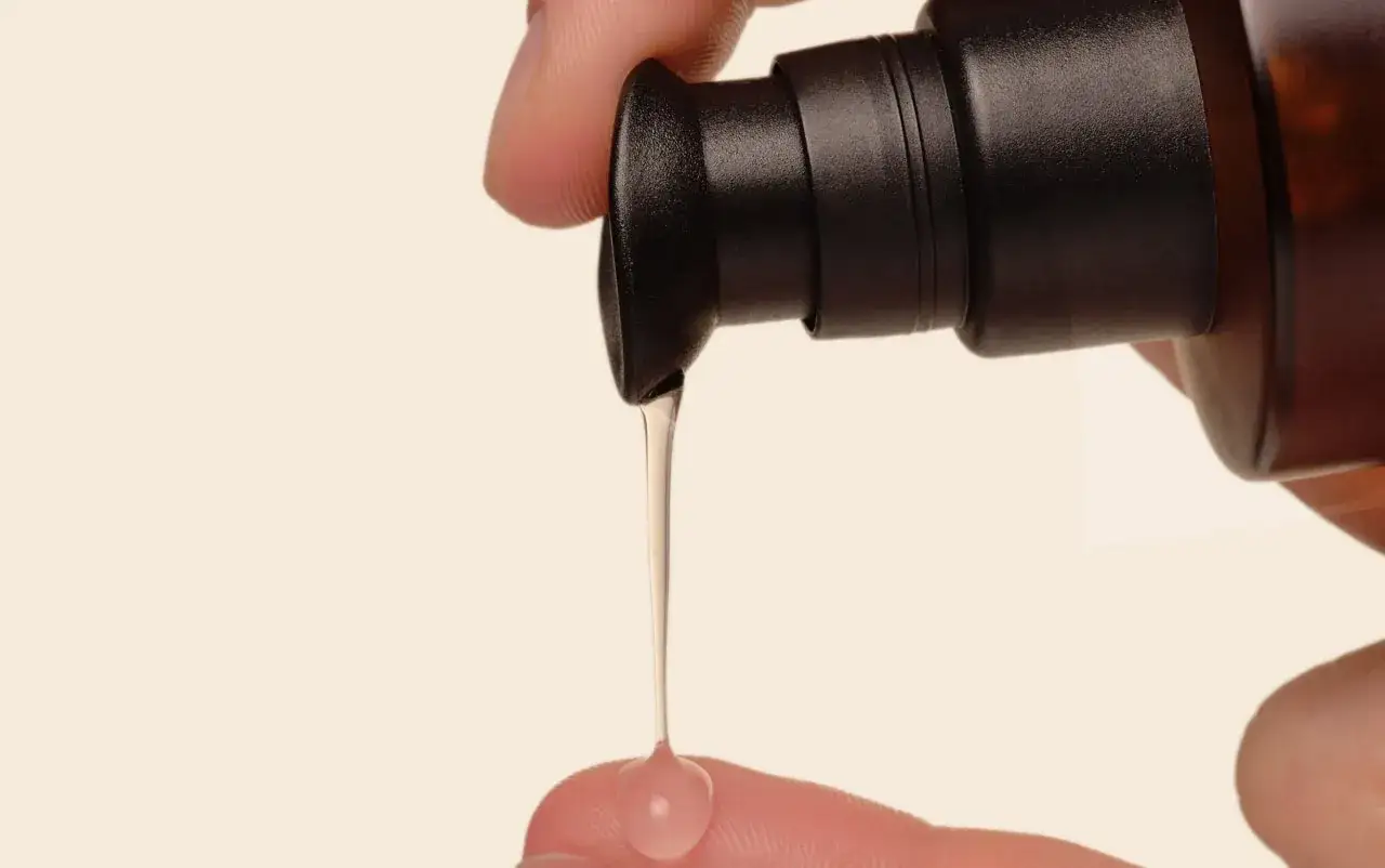 Un dito raccoglie una goccia di siero per capelli appena erogata da un flacone. Ideale per nutrire e proteggere.