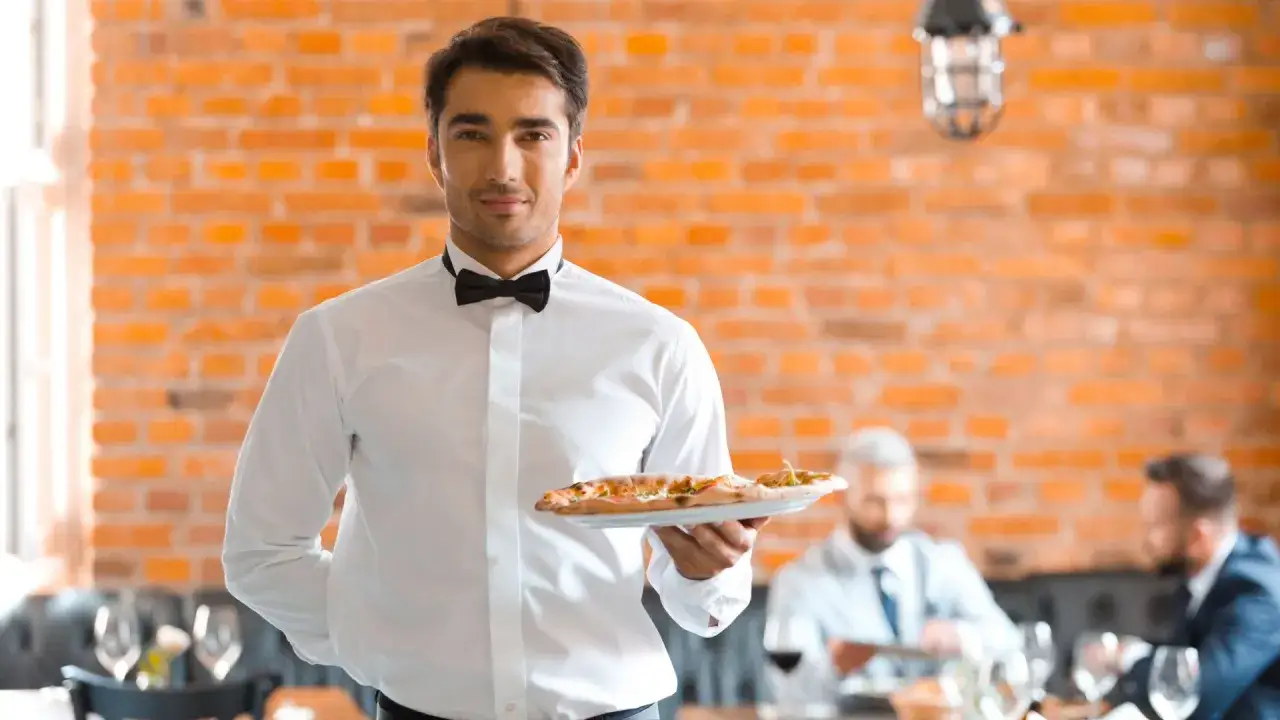 Elegancki kelner z pizzą zastanawia się, ile zarabia kelner za godzinę.